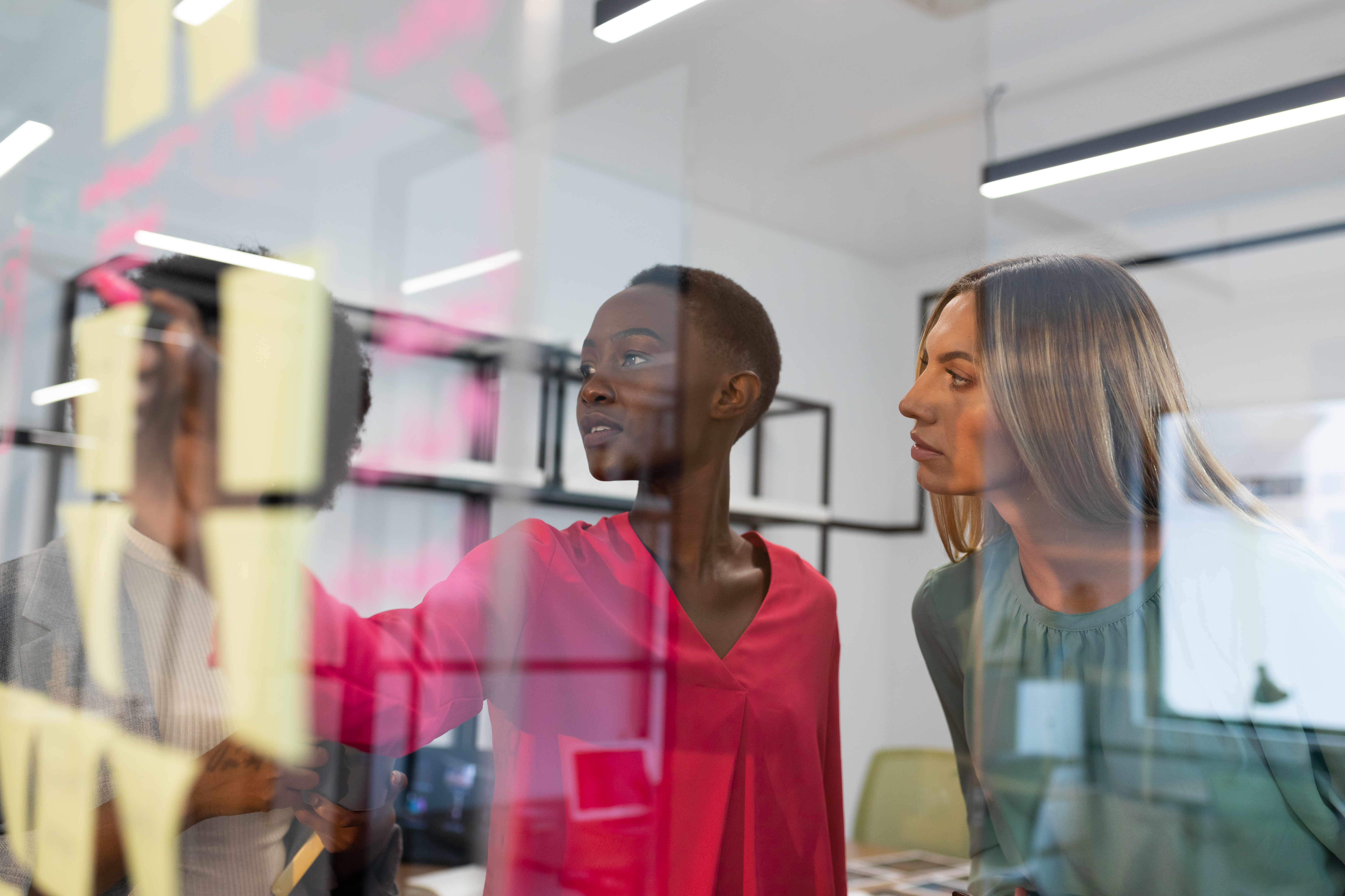 Diverse group of business colleagues brainstorming using glass wall in meeting room